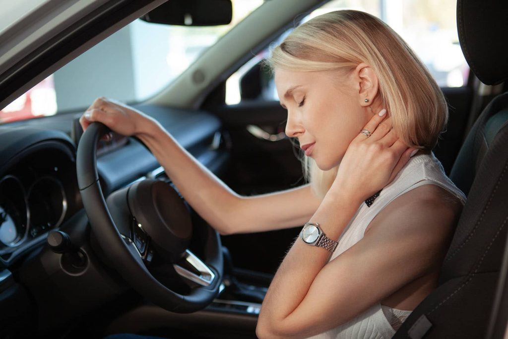 Female driver having neck and back pain from driving Beautiful blond haired woman rubbing her aching neck, sitting in her car. Female driver rubbing her neck, tired from driving
